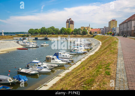 VUKOVAR, KROATIEN - 14. MAI 2018: Ein Blick auf die Boote an der Küste des Flusses Dunav mit Menschen zu Fuß auf die Promenade und das Hotel Dunav in t günstig Stockfoto