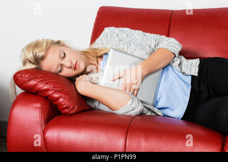 Eine schöne junge tausendjährigen Business woman Fang ein Nickerchen auf einem roten Sofa in einem Arbeitsplatz und hält Ihre Tablette; Sherwood Park, Alberta, Kanada Stockfoto