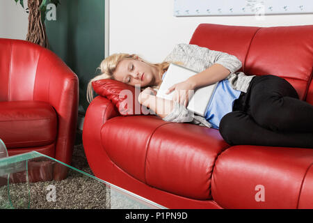 Eine schöne junge tausendjährigen Business woman Fang ein Nickerchen auf einem roten Sofa in einem Arbeitsplatz und hält Ihre Tablette; Sherwood Park, Alberta, Kanada Stockfoto