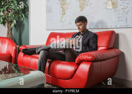 Junge tausendjährigen Geschäftsmann mit seinem Smart Phone in der Lobby eines Arbeitsplatz; Sherwood Park, Alberta, Kanada Stockfoto