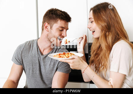 Fröhlicher junger Paare füttern sich gegenseitig mit Frühstück in einer Küche Stockfoto