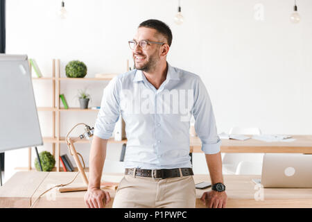 Happy Portrait von sachlich Mann mit weißem T-Shirt sitzen am Tisch im Büro und suchen mit dem Lächeln Stockfoto