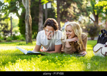 Ein junges Paar legt studieren auf dem Gras auf dem Campus der Universität durch ein Lehrbuch suchen und mit Hilfe eines Tablet; Edmonton, Alberta, Kanada Stockfoto