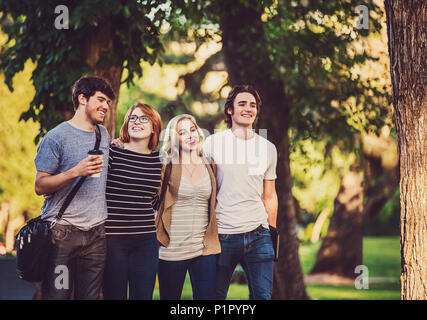 Eine Gruppe von vier Freunden zu Fuß eng zusammen Arm in Arm auf einen Weg beim Sprechen und Lachen auf dem Campus der Universität; Edmonton, Alberta, Kanada Stockfoto