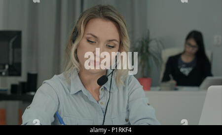 Call Center Mitarbeiter Notizen zu machen, während im Gespräch mit dem Kunden Stockfoto