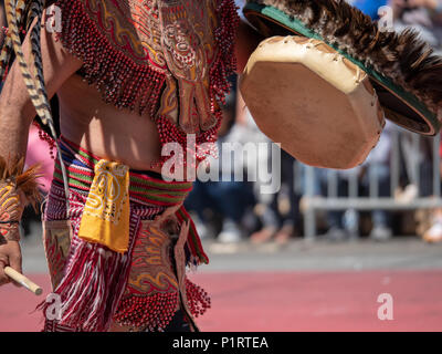 Ein Mann in der traditionellen Aztekischen Tracht Schläge auf einer Trommel während einer März gekleidet Stockfoto