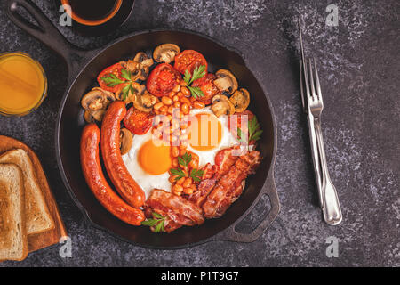 Traditionelles Englisches Frühstück mit Spiegelei, Würstchen, Bohnen, Pilze, gegrillten Tomaten und Speck. Ansicht von oben. Stockfoto