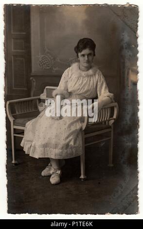 Deutschland - circa 1920s: Vintage Foto zeigt Frau sitzt auf einem weißen Zeitraum Bank. Retro black & white Studio. Stockfoto