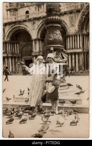 VENEZIA, ITALIEN - ca. 1926: Vintage Foto zeigt Frauen feed die Tauben auf dem Platz in Venezia. Frauen tragen cloche Hüte. Ferienhäuser Thema. Stockfoto