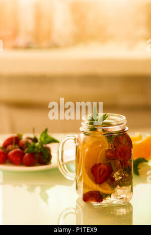 Stillleben mit einer Flasche in Scheiben geschnittene Orangen und Erdbeeren auf einem weißen Tisch, bio-veganen Milch Stockfoto