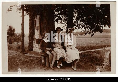 Die tschechoslowakische Republik - circa 1930s: Vintage Foto zeigt Frauen tragen elegante Kleider und Frauen parisisol großen Rand hat. Die Frauen und die jungen Stellen im Freien und auf der Bank sitzen. Retro Schwarz/Weiß-Fotografie. Stockfoto