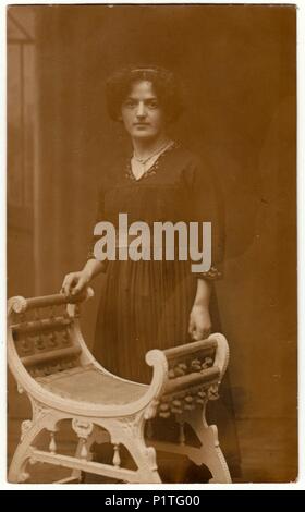 HAMBURG, DEUTSCHLAND, APRIL 1916: Vintage Foto zeigt eine junge Frau. Sie trägt ein schwarzes Kleid. Sie steht an einem historischen Stuhl. Retro black & white Studio. Stockfoto