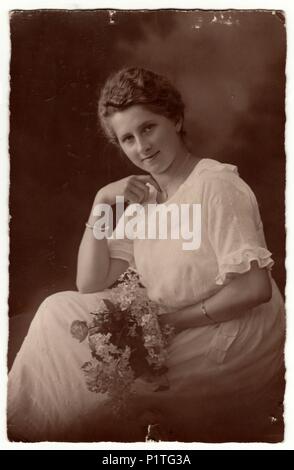 Deutschland - circa 1920s: photo Vintage zeigt Frau mit kurzen Haaren. Frau trägt weiße Kleid und hält Strauß (Blumen). Retro black & white Studio Fotografie mit Sepia Effekt. Stockfoto