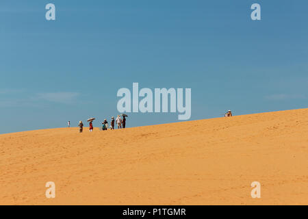 Mui Ne, Vietnam - Januar 2014: Gruppe von asiatischen Touristen mit Sonnenschirmen in der Wüste Landschaft/roten Sanddüne in Mui Ne, Vietnam Stockfoto