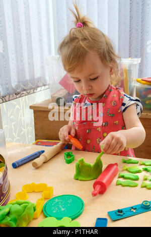 Spielerisch lernen. Glückliche junge zwei Jahre alte Mädchen spielen und Ausschneiden Modellierung Teig Ton. Stockfoto