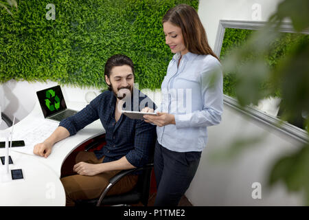 Clevere progressive junge Ingenieure arbeiten an digitalen Tablet auf einer ökologischen Bauvorhaben im Büro, reden über Windmühlen Projekt. Stockfoto