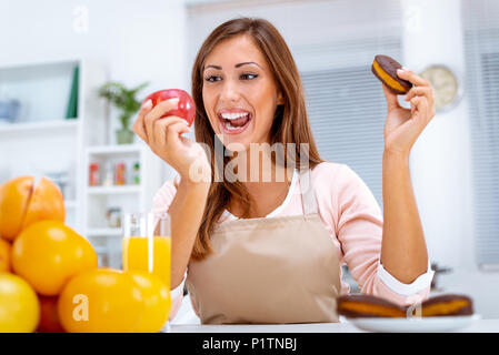 Schöne junge Frau in der Küche Entscheidung zwischen Apple und süße Schokolade Kuchen. Stockfoto