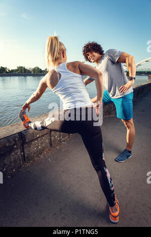 Junge glückliches Paar Training im Freien durch den Fluss, Stretching Beine bei Sonnenuntergang. Stockfoto