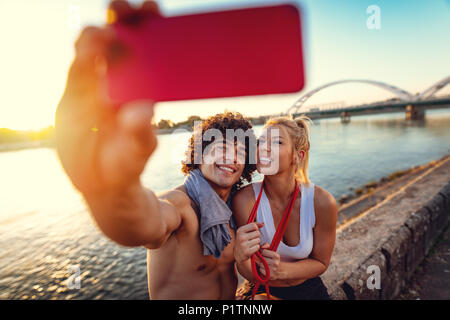 Schöne junge Paar ruht, lächelnd und selfie nach erfolgreicher Ausbildung durch den Fluss in den Sonnenuntergang. Stockfoto