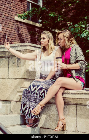 Zwei weibliche Studenten sitzen zusammen auf dem Campus ein Selbstporträt mit Ihrem Smart Phone und dumme pouty Lippen Stockfoto