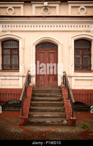 Nahaufnahme eines hölzernen Veranda mit einem braunen Tür und alte Fenster mit einem alten Haus ein Haus aus Stein, in Weiß und Rosa lackiert Stockfoto