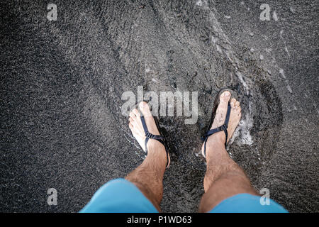 Life Balance Konzept. Man schaut auf die Füße und Schuhe an vulkanischen schwarzen Sandstrand entfernt. Beine entspannend, Laufen, Walken oder Joggen am Strand, inspir Stockfoto