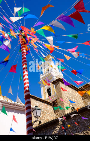 Sunlit Bunting und eine bunte Pole gegen eine Kirche Turm in einem kleinen spanischen Dorf während Fiesta. Stockfoto