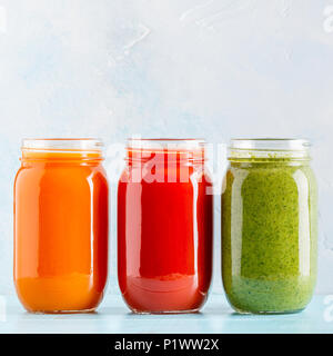 Orange/Grün/rot gefärbten Smoothies/Saft in einem Glas auf einem blauen Hintergrund. Stockfoto