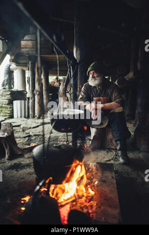 Alten bärtigen Förster mit Axt in der Nähe der Holzhütte Stockfoto