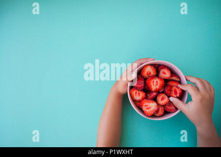 Child's Hände halten ein rosa Schüssel voll von schönen frischen saftigen Erdbeeren auf Pastell-blaue Hintergrund mit Text. Stockfoto