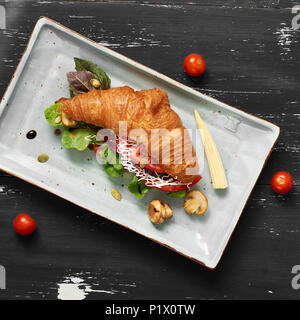 Lecker Sandwich aus Croissants gefüllt mit Gemüse, Salat, Pilzen und Sauce liegen auf flachen, rechteckigen Platte stehend auf Blau alte hölzerne Stockfoto