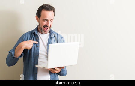 Älterer Mann mit Laptop Computer mit Überraschung Gesicht zeigenden Finger zu sich selbst Stockfoto
