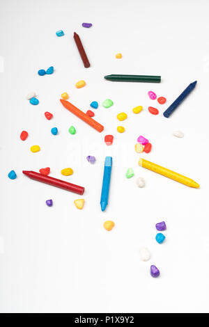 Einige farbige Buntstifte zwischen kleinen farbigen Steine auf eine weiße Fläche Stockfoto