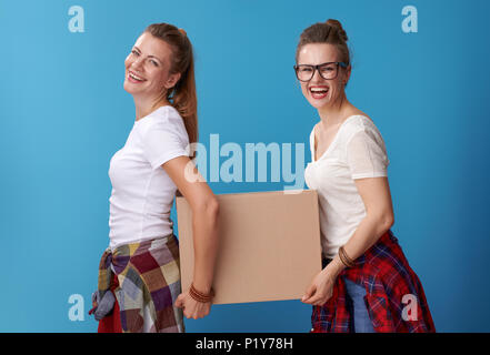 Lächelnd moderne hipster Mitbewohnern in weißen Hemden mit einem Karton zusammen auf blauem Hintergrund isoliert Stockfoto