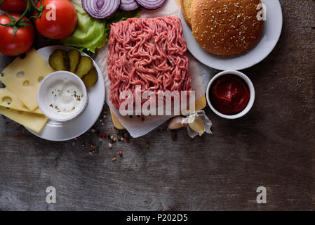 Rohes Hackfleisch auf Papier, Zutaten für Burger mit Tomaten, Zwiebeln und Gewürzen auf hölzernen Hintergrund Stockfoto