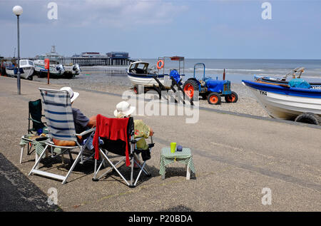 Senior Paar sitzen in Liegen, cromer Promenade, North Norfolk, England Stockfoto