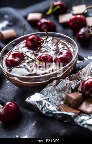 Frische Kirschen in der Schüssel mit Schokolade auf dunklen Tischdecke. Stockfoto
