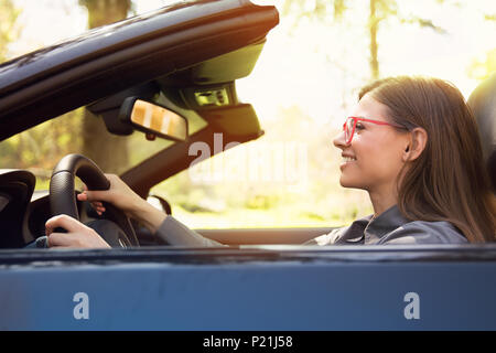 Geschossen von einer netten Frau genießen Sie die Fahrt in einem Cabrio durch einen Park oder den Wald lieben die Brise im Gesicht Stockfoto