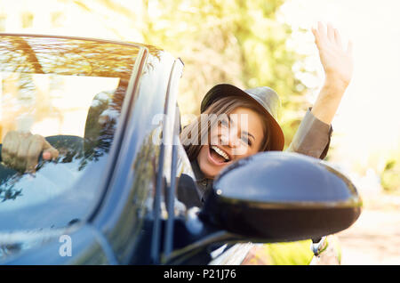 Schuss eine junge hübsche Frau genießen Sie die Fahrt in einem Cabrio liebe den Wind in Ihrem Gesicht wedelte mit ihrem Arm Stockfoto