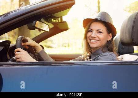 Geschossen von einer netten Frau genießen Sie die Fahrt in einem Cabrio durch einen Park oder den Wald lieben die Brise im Gesicht Stockfoto