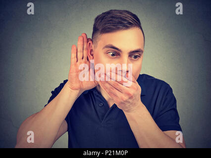 Junger Mann die Hand in der Nähe des Ohrs hören Klatsch und deckt Mund von Staunen Stockfoto