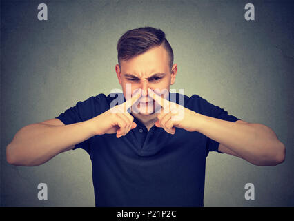 Man drückt mit den Fingern die Nase schaut mit Ekel etwas stinkt auf grauem Hintergrund. Stockfoto