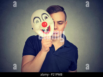 Traurig und deprimiert Mann das Gesicht mit Happy clown Maske seine Persönlichkeit verstecken. Stockfoto