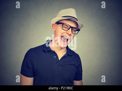 Fröhlicher junger Mann, der in einem weißen Hut über graue Wand Hintergrund winking Stockfoto