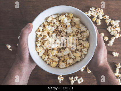 Hände, die Schüssel mit Popcorn über Holz- Tabelle ausgefüllt Stockfoto