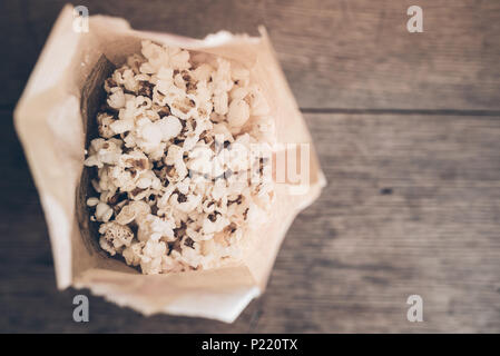 Ansicht von oben frisches Popcorn in der braunen Papiertüte auf rustikalen Holztisch Stockfoto