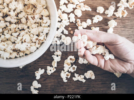 Nahaufnahme einer Hand, die Popcorn oben Holztisch Stockfoto