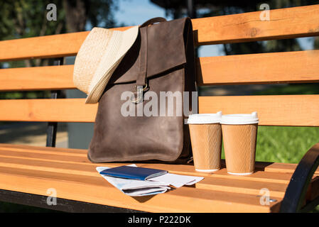 Nahaufnahme der braunen Ledertasche mit Hut, Reisepass mit Tickets, Karte und Pappbecher auf holzbank Stockfoto