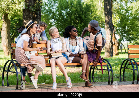 Multikulturelle Gruppe von Studenten, die auf der Werkbank zusammen ruhen in Park Stockfoto