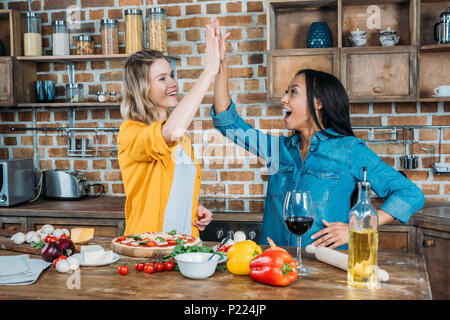 Fröhlicher junger miltiehnic Frauen hoch fünf beim Kochen in der Küche Stockfoto